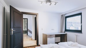 Une chambre d’hôtel avec un lit, un bureau, une fenêtre et une porte donnant sur un escalier.