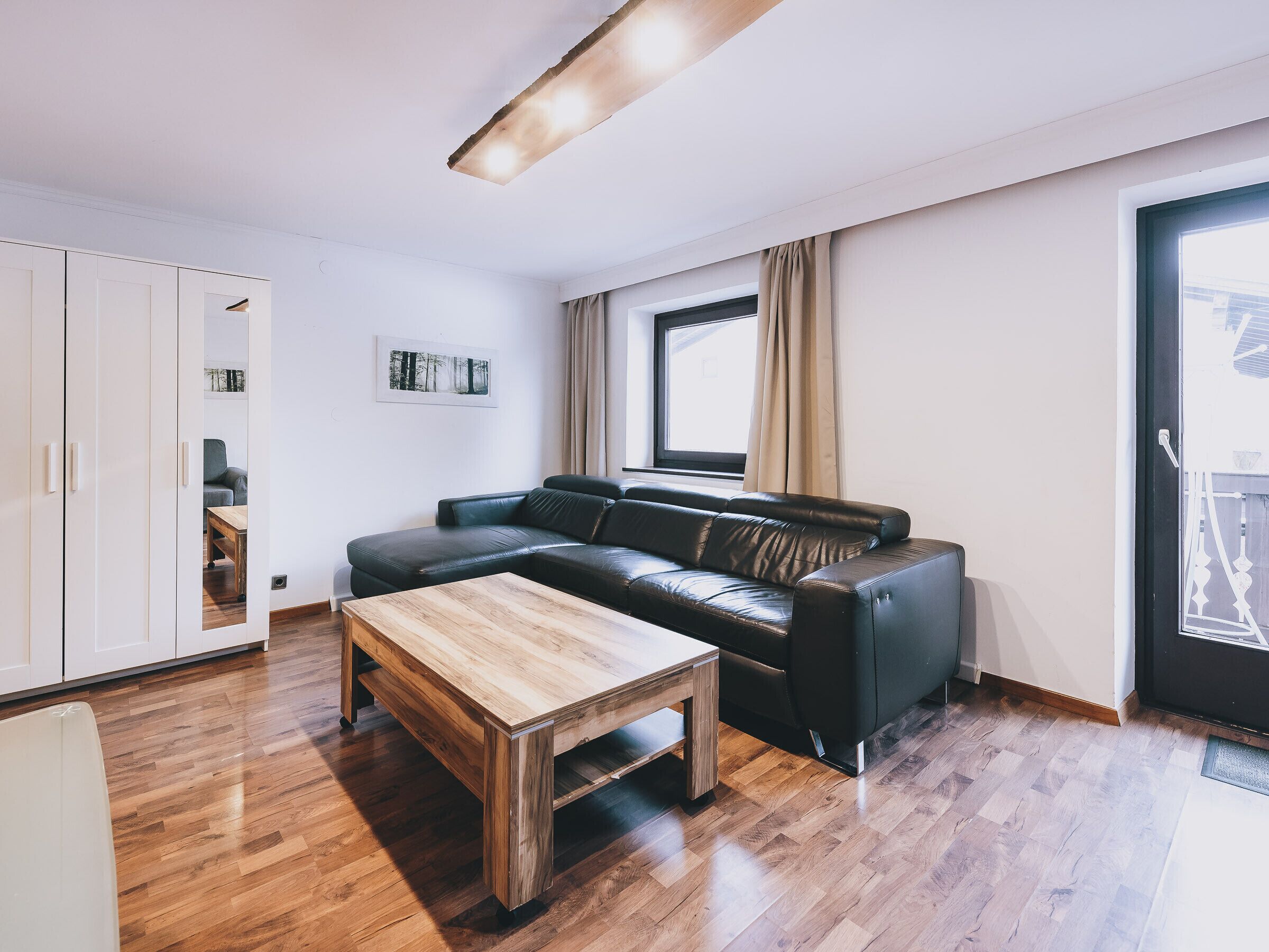 A modern living room with a leather sofa, wooden coffee table, and a large window with curtains.