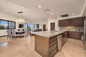 Une cuisine moderne dotée d’un grand îlot central, de meubles en bois foncé et d’un coin repas avec des chaises et une table.