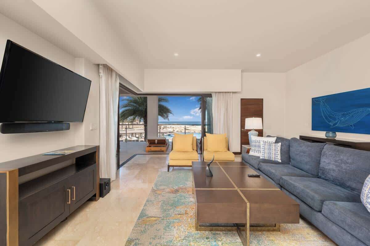 A modern living room with a flat-screen TV, a sofa, a coffee table, and a view of the ocean.