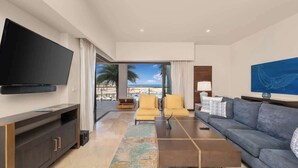 A modern living room with a flat-screen TV, a sofa, a coffee table, and a view of the ocean.