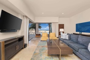 A modern living room with a flat-screen TV, a sofa, a coffee table, and a view of the ocean.