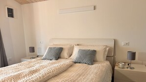 Un lit bien fait, recouvert d’une couverture à motifs, avec deux oreillers, une table de chevet dotée d’une lampe et un interrupteur fixé au mur.