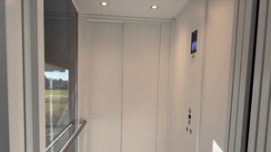 Un ascenseur doté d’un écran numérique, d’une porte en verre et d’une main courante en métal.