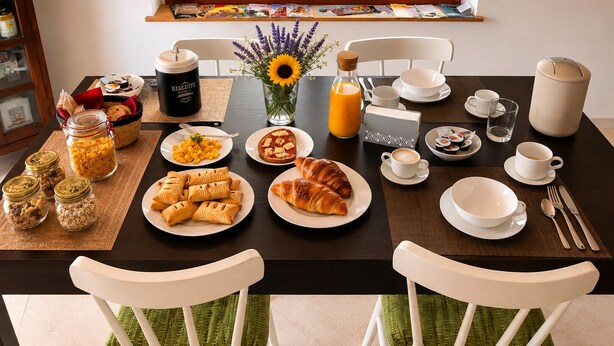 Une table mise pour le petit-déjeuner, avec une nappe pour deux personnes, comprenant des assiettes remplies de nourriture, une tasse de café et un vase avec des fleurs.