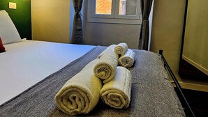 Una cama bien hecha con toallas enrolladas, una ventana con cortinas y vista a un edificio.