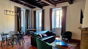 Un amplio salón con techo alto, vigas a la vista, una mesa de comedor con sillas, un sofá y una pequeña mesita auxiliar.