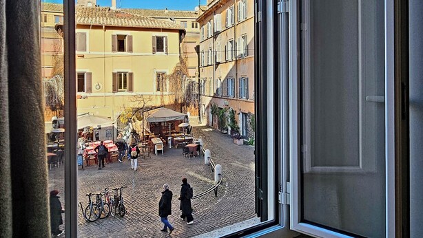 Une vue depuis une fenêtre donnant sur une rue pavée, avec des bâtiments, un café et des vélos.