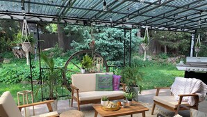 A covered patio area with outdoor furniture, hanging planters, and a grill.