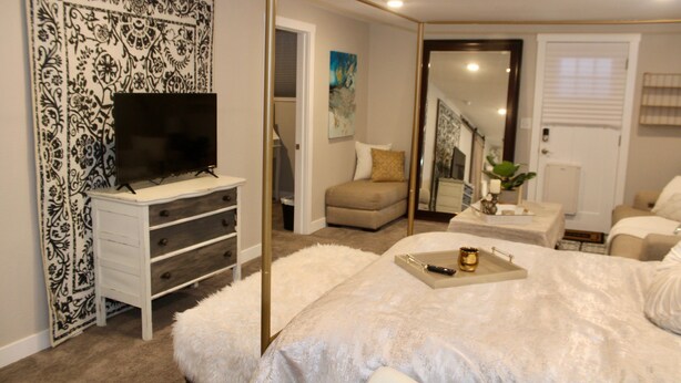 A bedroom with a large bed, a TV on a dresser, a mirror, and a door leading to a staircase.