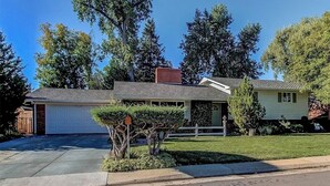 A single-story house with a garage, a front lawn, and mature trees.