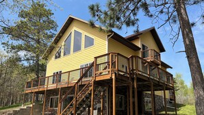 Une maison à deux étages dotée d’une terrasse en bois et d’un escalier menant à un balcon.
