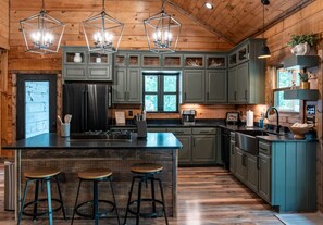 A spacious kitchen with a central island, wooden flooring, and green cabinets. - All Decked Out-Pet Friendly, Luxury Log Cabin Rental, High Speed Internet, 4 Decks, Swinging Day Bed, Large Hot Tub-Nantahala NC. (Topton)