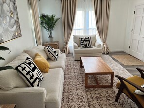 Un soggiorno con un divano color beige, un tavolino in legno e una poltrona gialla. Si nota una pianta in vaso e un quadro appeso al muro.
