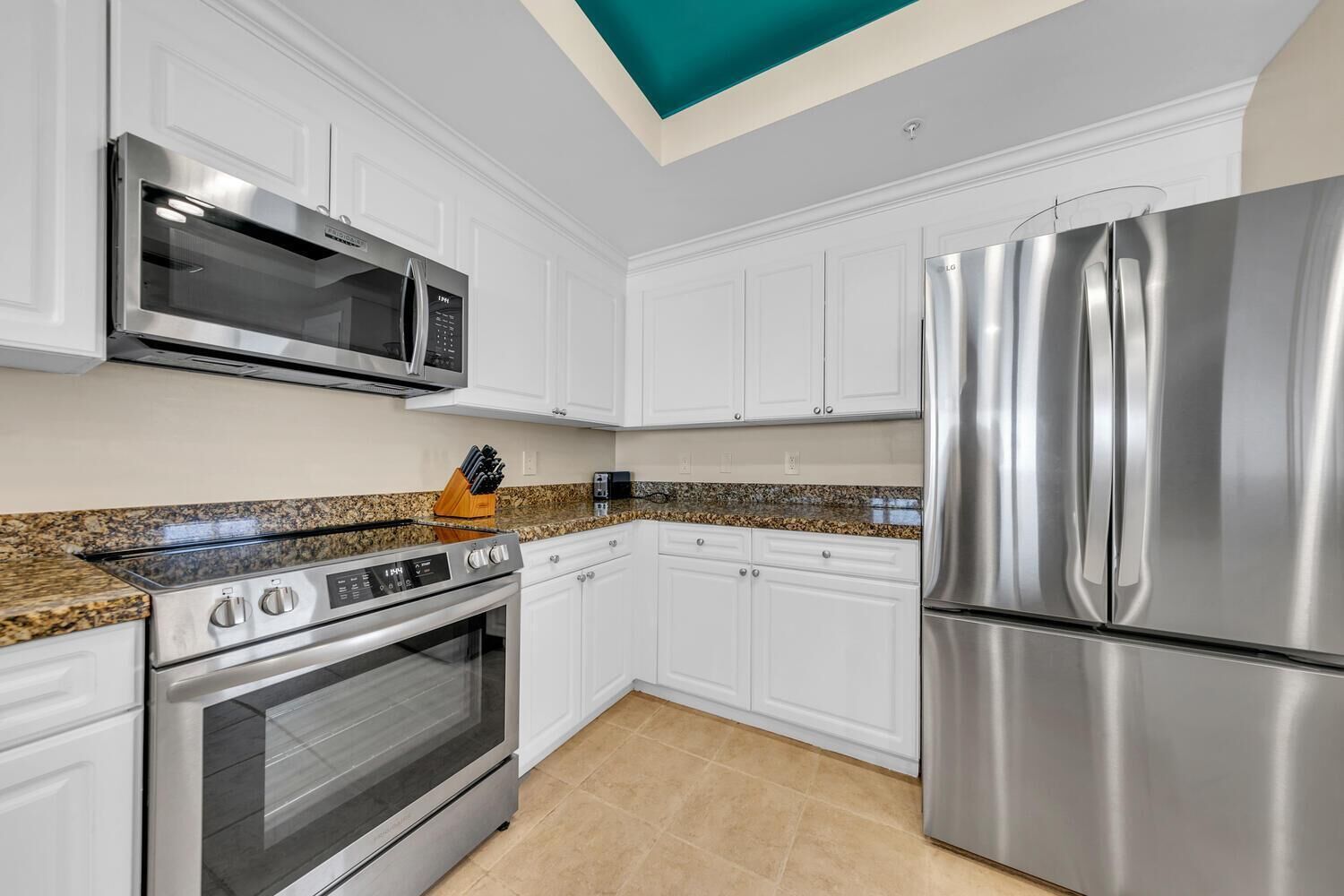 A modern kitchen with white cabinets, stainless steel appliances, granite countertops, and a skylight.