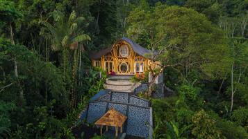 A luxurious villa surrounded by lush greenery, featuring a central courtyard with a stone mosaic floor and a small thatched-roof structure.