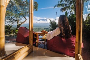 A person seated on a wooden bench with a view of a mountainous landscape.