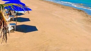 A beach with clear blue water, a sandy shore, and blue umbrellas. - Pousada Bangalôs Do Pontal (Japaratinga)