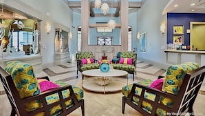 A spacious lobby with a high ceiling, a central round table, and colorful patterned chairs.