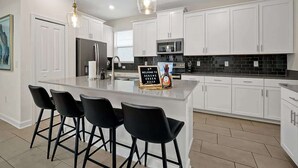 A modern kitchen with white cabinets, a central island with bar stools, and a sign welcoming guests.