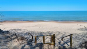A beach with a wooden bench and a clear view of the ocean.