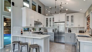 A modern kitchen with white cabinetry, a stainless steel refrigerator, and a large island with stools.