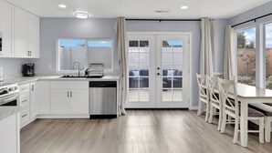 A modern kitchen with white cabinets, a dishwasher, and a dining area with a table and chairs. - Entire house near Monterey with Jacuzzi (Salinas)