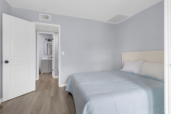 A bedroom with a bed, a door leading to a bathroom, and a hallway.