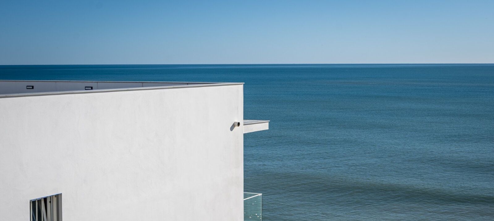 A white building with a flat roof overlooking a calm sea.