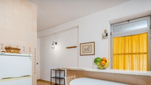 A compact kitchen with a refrigerator, a small dining table, and a window with yellow curtains. - #258 Travessa do Mar F by Home Holidays (Albufeira)