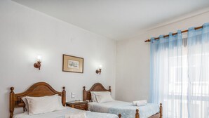 A hotel room with two wooden beds, a nightstand, a framed picture on the wall, and sheer blue curtains. - #258 Travessa do Mar F by Home Holidays (Albufeira)