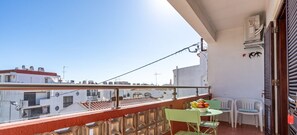 Un balcon avec une table et des chaises, un panier de fruits et une vue sur les bâtiments.