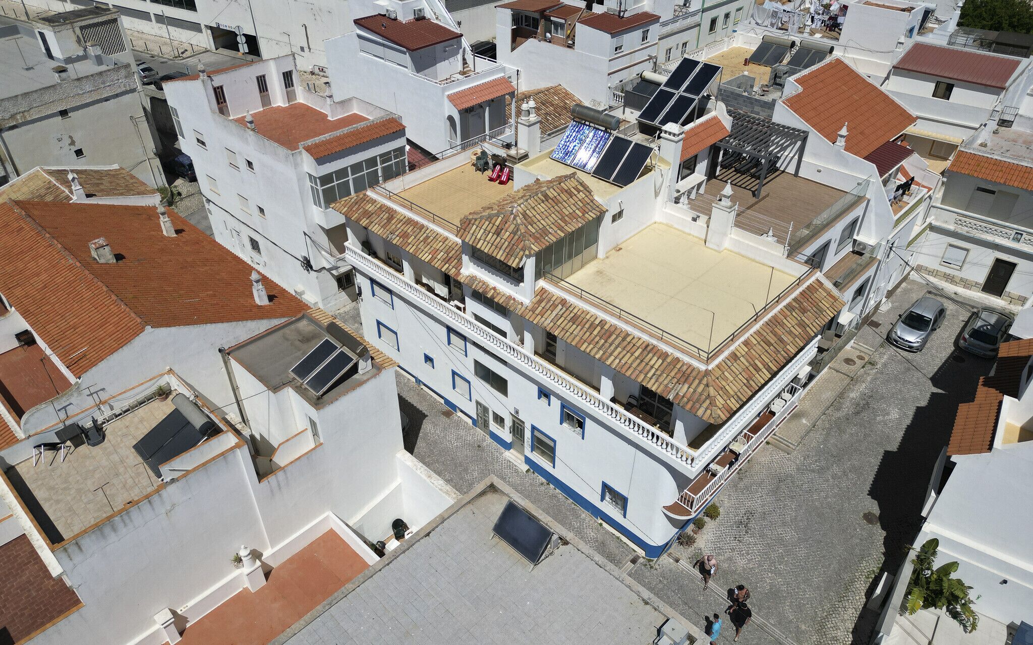 A white building with a tiled roof, multiple windows, and a flat rooftop area.