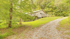 A house with a deck, surrounded by trees and a gravel path. - Peaceful Cabin at Lake Logan w/ Spacious Yard! (Ardmore)