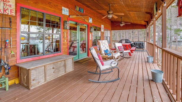 Een houten terras met schommelstoelen, een barbecue en een bord waarop staat 'GO JUMP THE LAKE'.