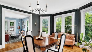 Una sala da pranzo con un tavolo e sedie in legno, un lampadario e vista sull'esterno.