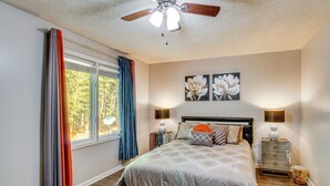 Un dormitorio con cama, cortinas, ventilador de techo, mesita de noche con lámpara y decoración en la pared.