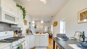 Una cocina moderna con armarios blancos, una isla central y una zona de comedor con una mesa de madera oscura.
