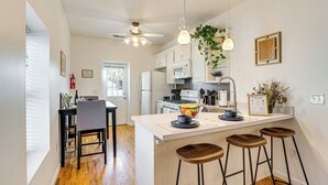 Una cocina moderna con armarios blancos, una isla central con taburetes, un ventilador de techo y plantas colgantes.