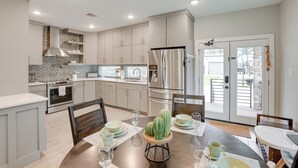 A modern kitchen with stainless steel appliances, a dining area with a wooden table, and a view of the outdoor patio through glass doors. - Pets Welcome: Home w/ Deck & Patio in Hockley! (Hockley)