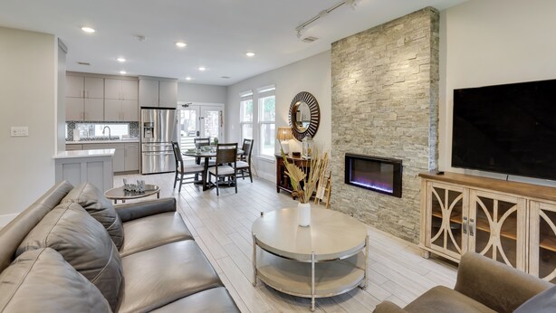A modern living room with a stone accent wall, a flat-screen TV, and a dining area with a kitchen in the background. - Pets Welcome: Home w/ Deck & Patio in Hockley! (Hockley)