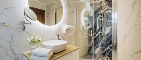 A modern bathroom with a marble vanity, a glass shower enclosure, and a round mirror.
