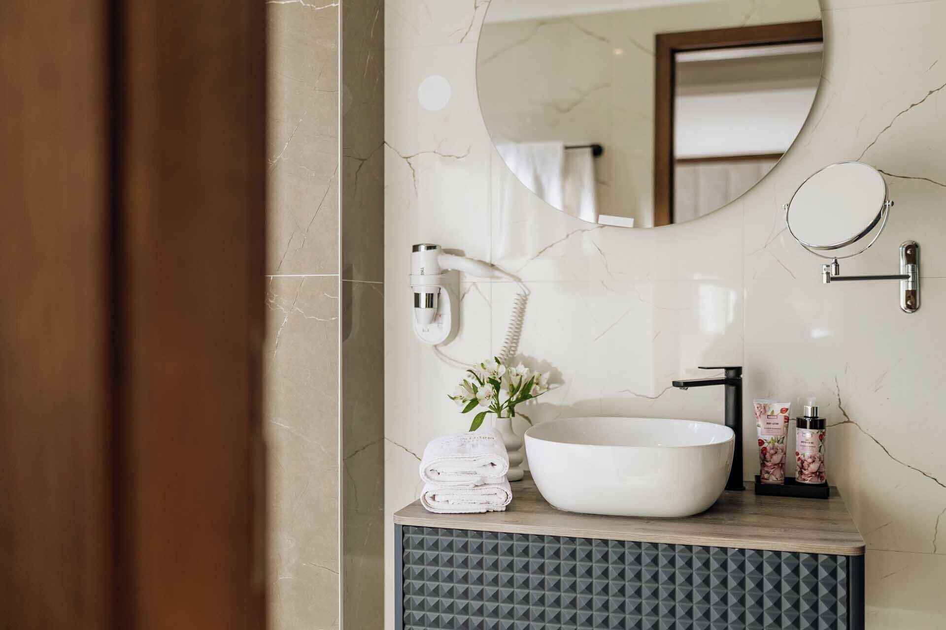 Un baño con un lavamanos blanco, un espejo y un perchero para toallas.