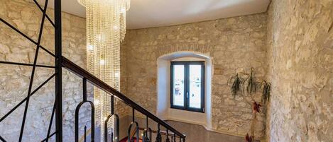 A staircase with a red carpet, a chandelier, and a stone wall.