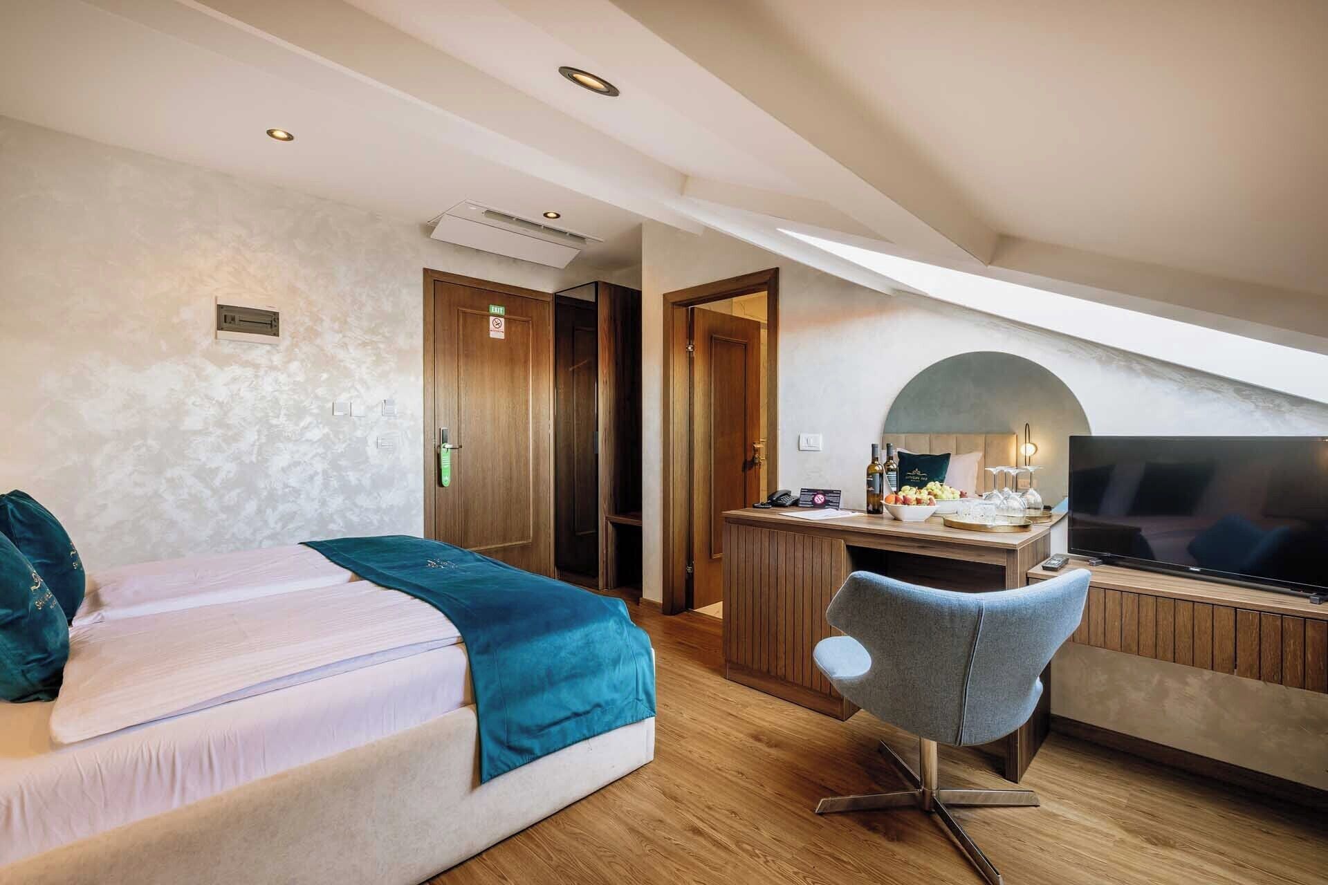 A modern hotel room with a bed, a desk with a TV, and a chair.