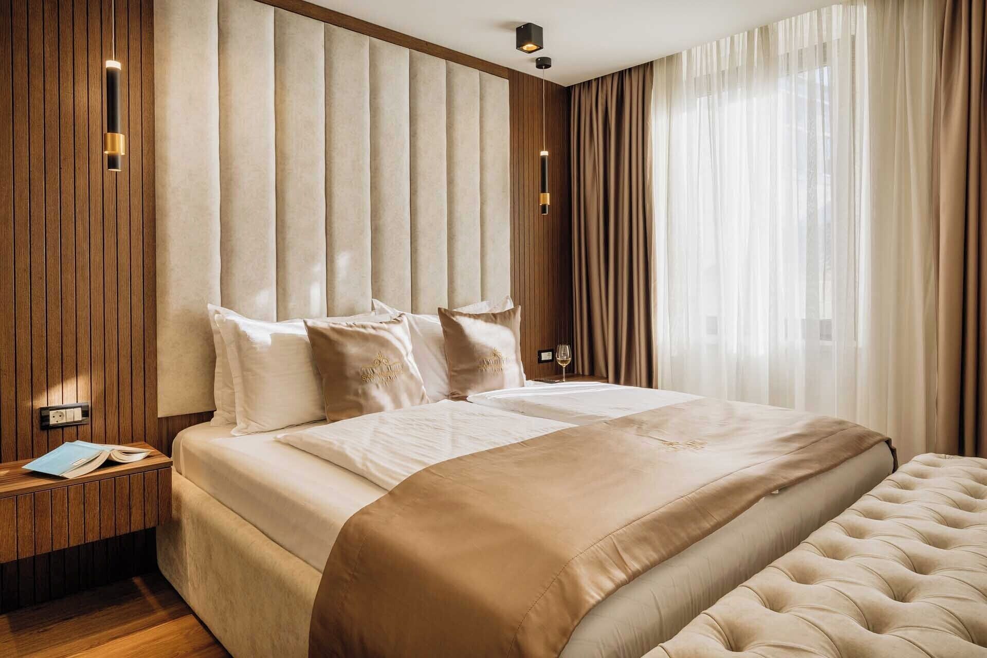 Ett hotellrum med en stor säng, träpanel på väggarna och ett fönster med tunna, genomskinliga gardiner.