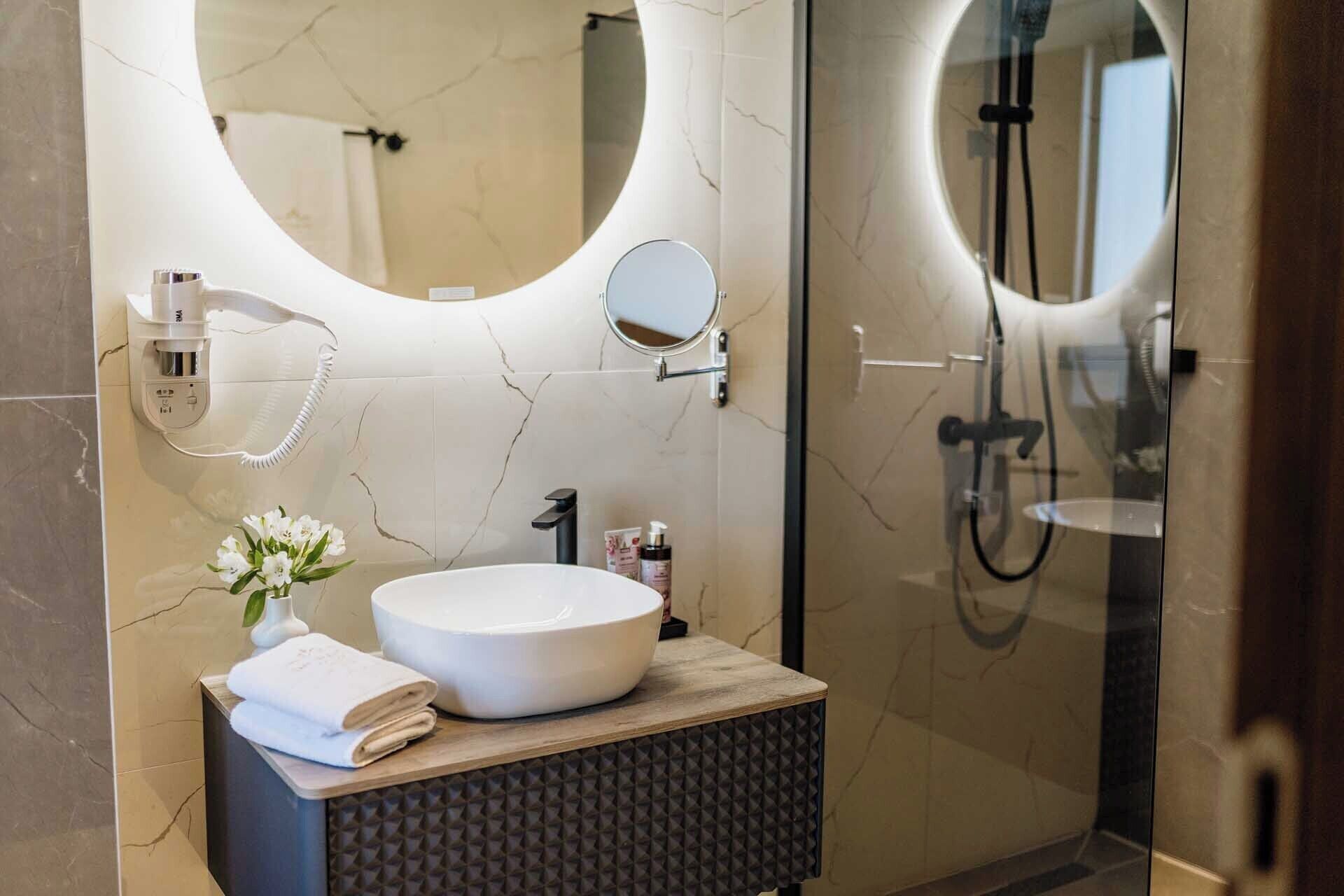 A modern bathroom with a round mirror, a white sink, and a handheld showerhead.