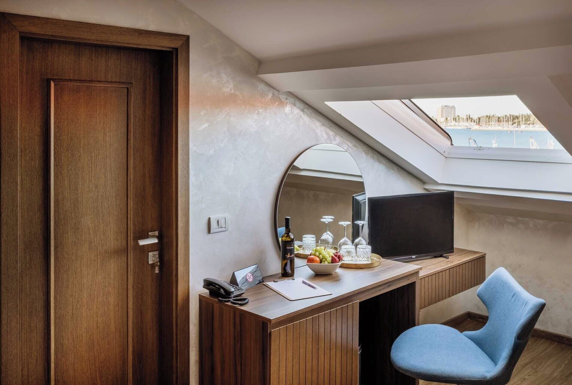 A room with a wooden desk, a television, a mirror, and a skylight.