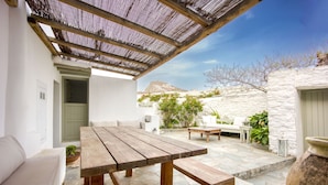 Eine Terrasse im Freien mit einem Holztisch und Bänken, einem weißen Sofa und einem Steinfußboden.