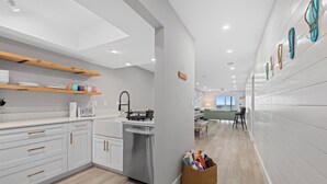 A modern kitchen with white cabinetry, wooden shelves, and a stainless steel dishwasher.